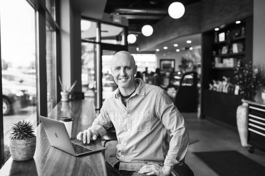 Photograph of Brian Gardner at a coffee bar with his laptop open.