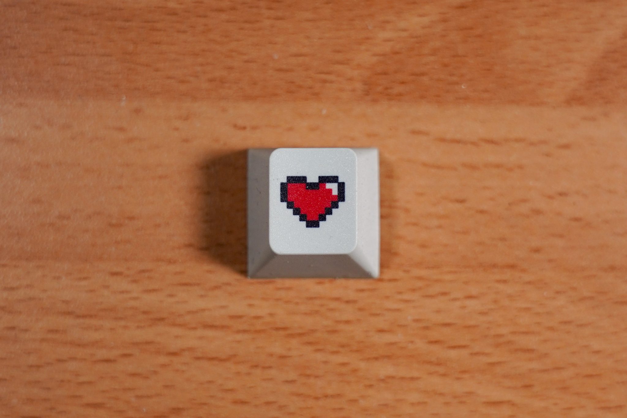 Computer key cap with a pixel-art heart on a wooden table.