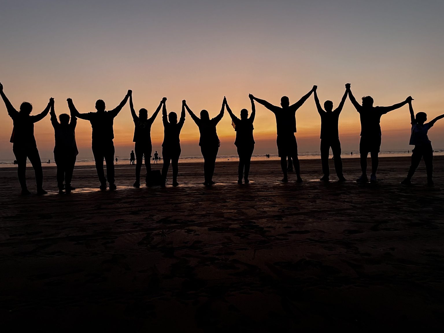 10 people in a line holding hands on a beach.